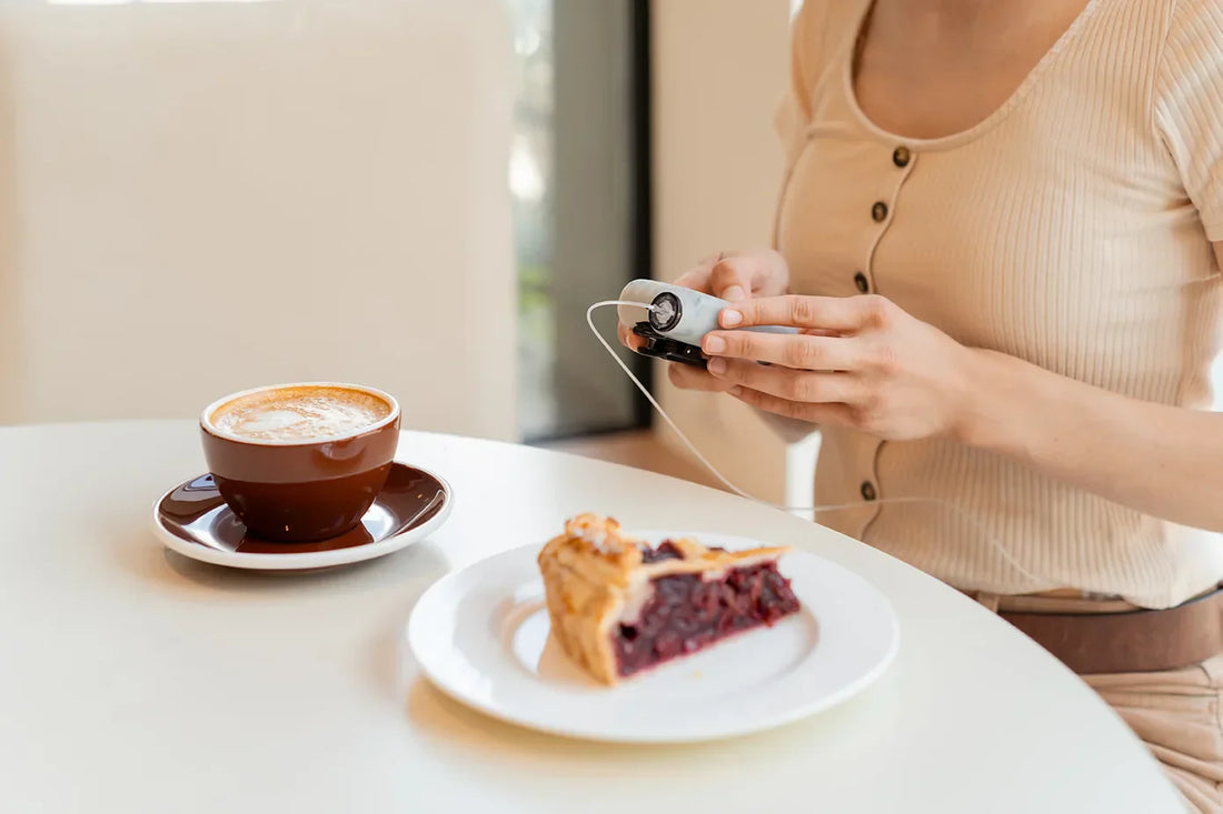 Frau misst ihren Blutzucker - während ein Stück Kuchen und eine Tasse Kaffee vor ihr stehen
